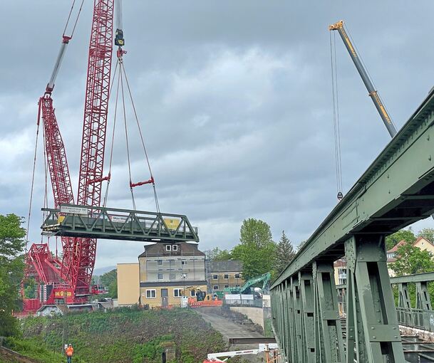 Szenen eines Abschieds: Ein Kran wuchtet ein Teil der Großen Pflugfelder Brücke in die Höhe. Links schweißen Arbeiter an der grünen Stahlkonstruktion. Rechts eine Skizze des Neubaus.