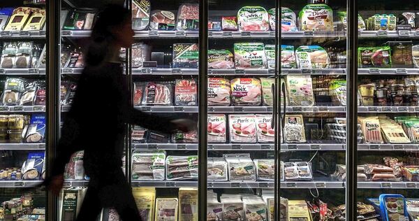Eine Person geht vor einem Kühlregal im Supermarkt entlang. Eine Person geht vor einem Kühlregal im Supermarkt entlang.