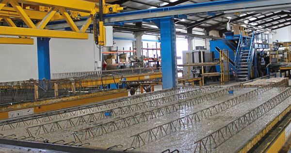 Eine Werkhalle mit Anlagen, auf denen Elementdecken hergestellt werden. Die Fertigung von Betonbauteilen im Werk unterscheidet s Eine Werkhalle mit Anlagen, auf denen Elementdecken hergestellt werden. Die Fertigung von Betonbauteilen im Werk unterscheidet sich zum Einsatz von Transportbeton, der auf die Baustelle transportiert und vor Ort verarbeitet wird.