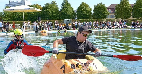 Viele Menschen haben zugeschaut, als Männer und Frauen in Riesenkürbissen über den See gepaddelt sind. Viele Menschen haben zugeschaut, als Männer und Frauen in Riesenkürbissen über den See gepaddelt sind.